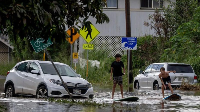 Two teenagers surf next to a disabled vehicle in flood water in Waialua, Hawaii on Friday.