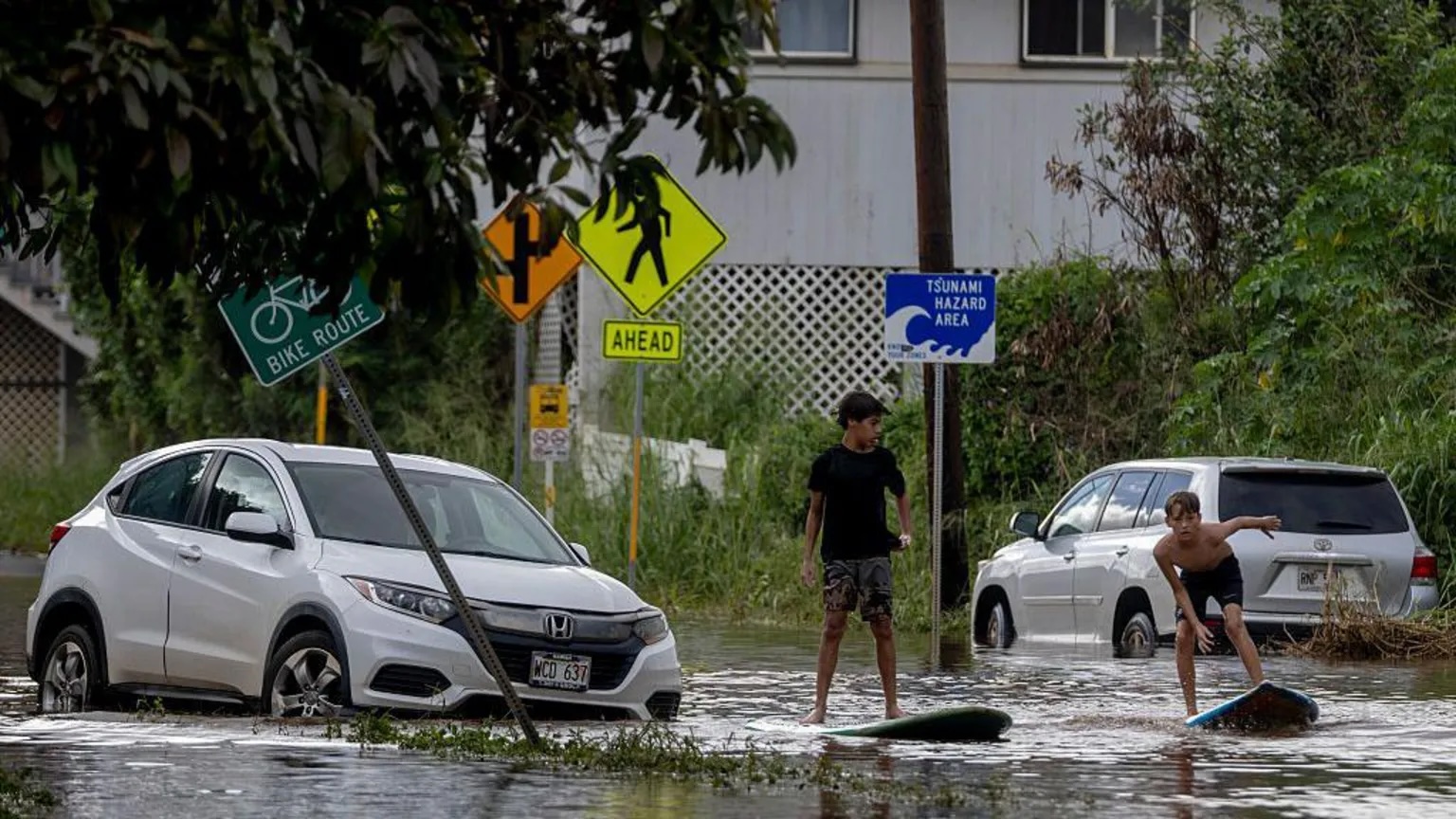 Two teenagers surf next to a disabled vehicle in flood water in Waialua, Hawaii on Friday.