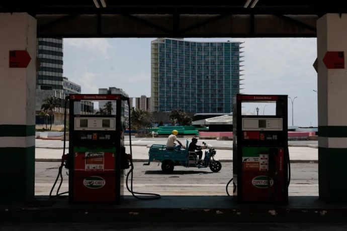 An electric tricycle driver passes in front of a gas station in Havana, Cuba.